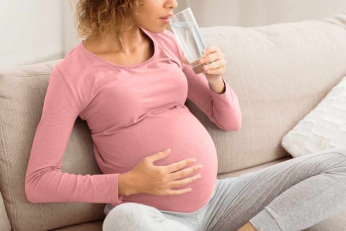Pregnant,Woman,Drinking,Water,Sitting,On,Sofa,,Resting,At,Home.