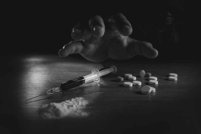 A hand reaching for pills next to a syringe and powder on a table