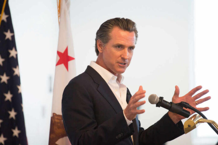A man in a suit speaking into a microphone with a California flag in the background