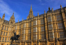 The Palace of Westminster with a statue in the foreground under a blue sky