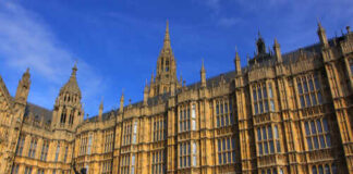 The Palace of Westminster with a statue in the foreground under a blue sky