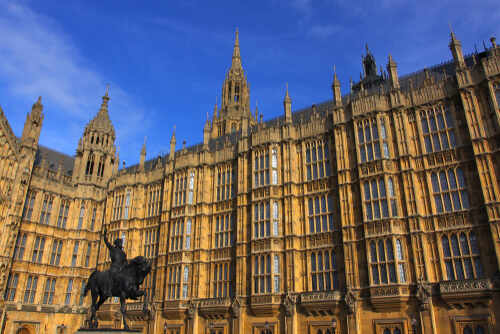 The Palace of Westminster with a statue in the foreground under a blue sky