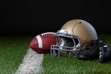 A football helmet, a football, and cleats on a field