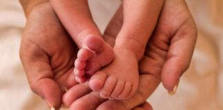 A close-up of a babys feet being held gently in adult hands