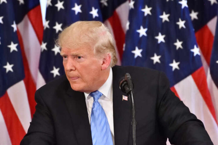 shutterstock_1277074255.jpg A man in a suit speaking at a podium with American flags in the background