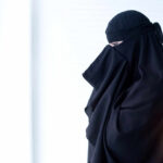 Woman wearing a black abaya, partially turned to the side