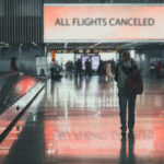 Stranded Americans Scramble—Airspace Shut A lone passenger standing in an airport terminal with a sign indicating all flights are canceled