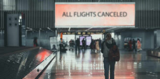 A lone passenger standing in an airport terminal with a sign indicating all flights are canceled