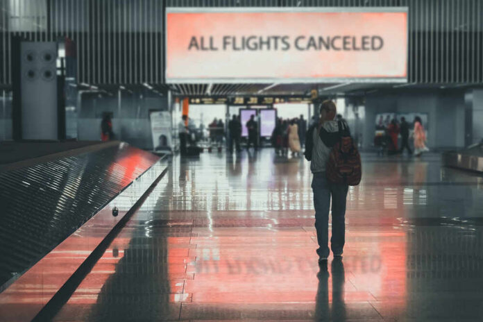 A lone passenger standing in an airport terminal with a sign indicating all flights are canceled