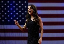 A woman passionately speaking at a podium with an American flag backdrop