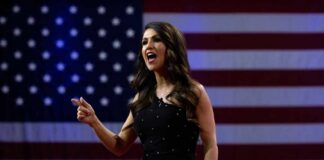 A woman passionately speaking at a podium with an American flag backdrop