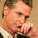 Condescending Gavin Newsom CAUGHT — He Said WHAT?! Close-up of a man in a suit with a thoughtful expression, hand on chin
