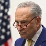 Stunning Schumer Flip-Flop on Election Integrity A serious-looking man in a blue suit with glasses, standing near an American flag