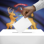 Hand placing a ballot into a ballot box with the Michigan state flag in the background