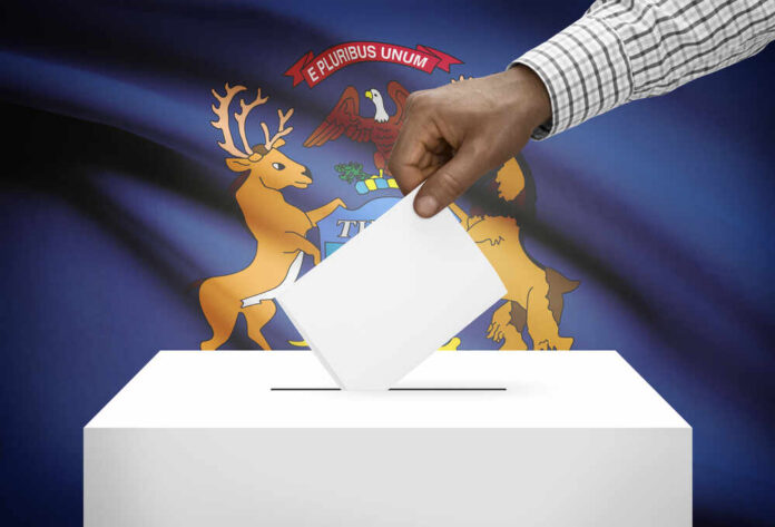 shutterstock_244411453.jpg Hand placing a ballot into a ballot box with the Michigan state flag in the background