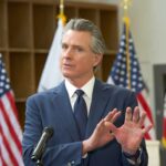 Newsom’s Transparency Law BACKFIRES – Major Cost! A government official speaking at a podium with American flags in the background