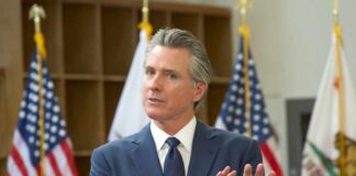 A government official speaking at a podium with American flags in the background