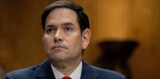 A government official sitting at a hearing table with a serious expression