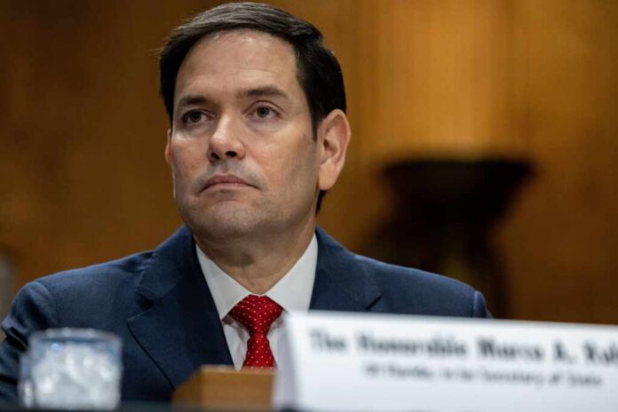 A government official sitting at a hearing table with a serious expression