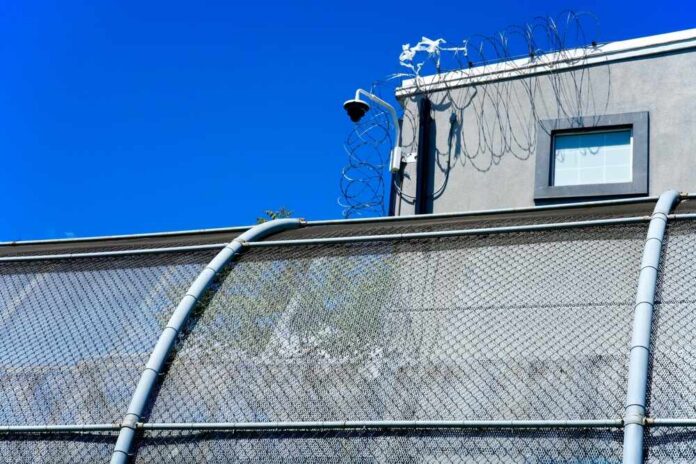 Security camera mounted above a prison fence with barbed wire against a blue sky