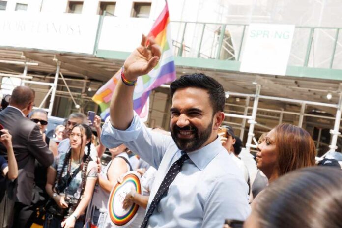 shutterstock_2649528781.jpg Smiling man waving at a pride parade with a rainbow flag in the background