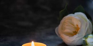 A lit candle next to a white flower arrangement on a dark surface