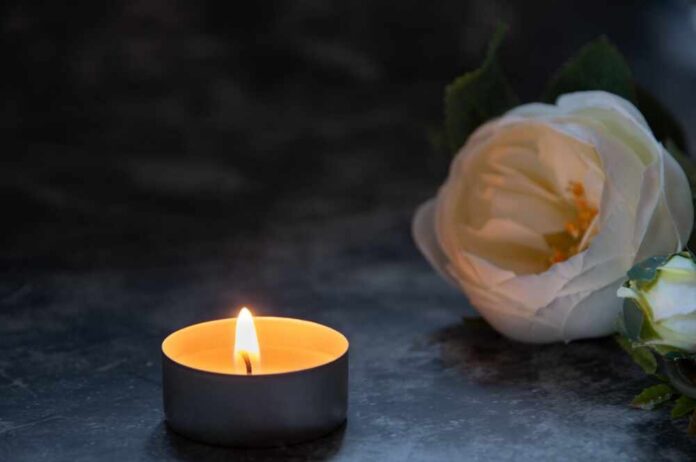 A lit candle next to a white flower arrangement on a dark surface