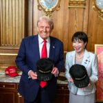 Two individuals holding hats with 'JAPAN IS BACK' text in a formal setting