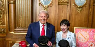 Two individuals holding hats with 'JAPAN IS BACK' text in a formal setting