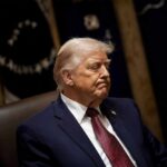 Trump SLAMS Reporter on Air Force One – SHOCKING! A political figure seated with a serious expression in a formal setting