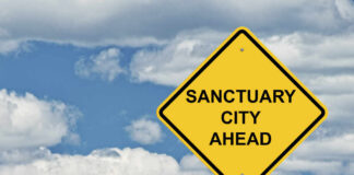 Yellow road sign indicating a sanctuary city ahead against a blue sky