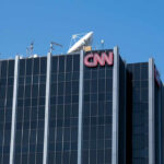 The top of the CNN building featuring the logo and broadcasting equipment against a clear blue sky