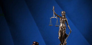 Bronze statue of Lady Justice holding scales next to a gavel on a book
