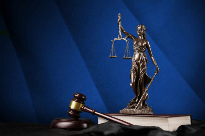 Bronze statue of Lady Justice holding scales next to a gavel on a book