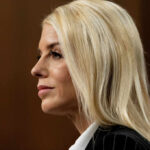 Profile view of a woman with blonde hair in business attire, displaying a serious expression