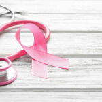A pink ribbon next to a stethoscope on a wooden surface