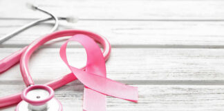 A pink ribbon next to a stethoscope on a wooden surface