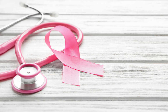 A pink ribbon next to a stethoscope on a wooden surface