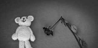 A crocheted teddy bear next to a wilted rose on a textured surface