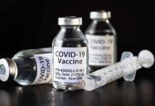 Vials of COVID-19 vaccine and a syringe on a dark background
