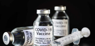 Vials of COVID-19 vaccine and a syringe on a dark background