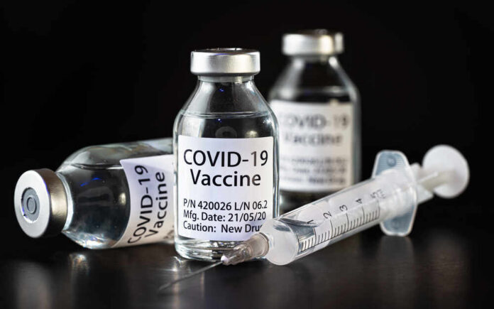 shutterstock_1764806555.jpg Vials of COVID-19 vaccine and a syringe on a dark background