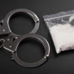 Handcuffs next to a bag of white powder on a dark surface