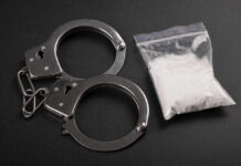 Handcuffs next to a bag of white powder on a dark surface
