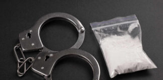 Handcuffs next to a bag of white powder on a dark surface