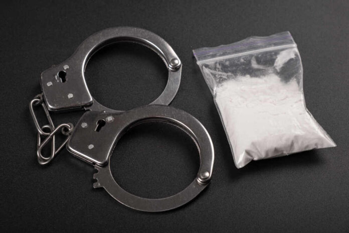 Handcuffs next to a bag of white powder on a dark surface