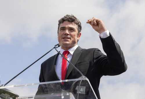 Man in a suit delivering a speech at an outdoor event