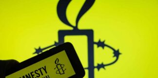 A hand holding a mobile device displaying the Amnesty International logo against a yellow background