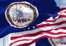 Governor Hijacks Predecessor’s Success? Critics Cry Foul Virginia state flag waving in the foreground with an American flag in the background