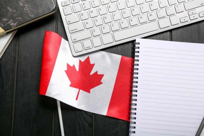 Canadian flag placed on a desk next to a keyboard and a blank notebook